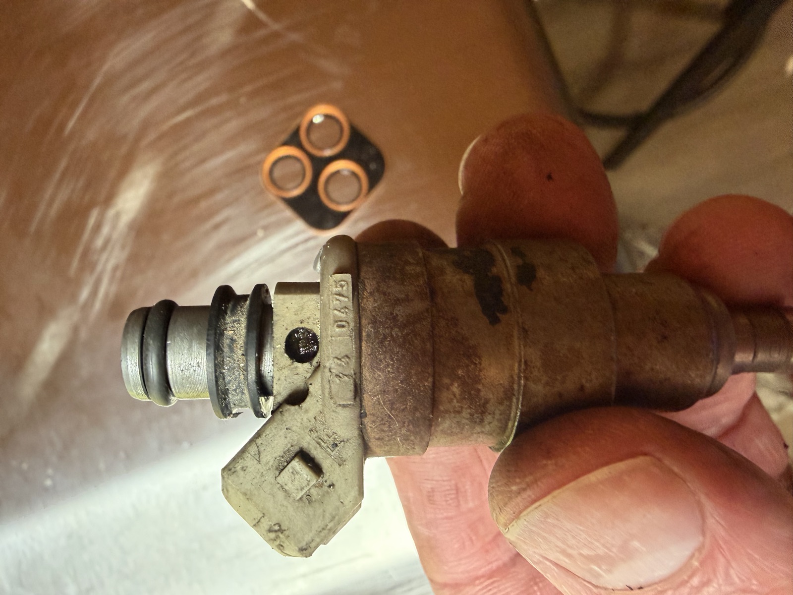 An automotive fuel injector before cleaning, caked in carbon and varnish with worn o-rings removed